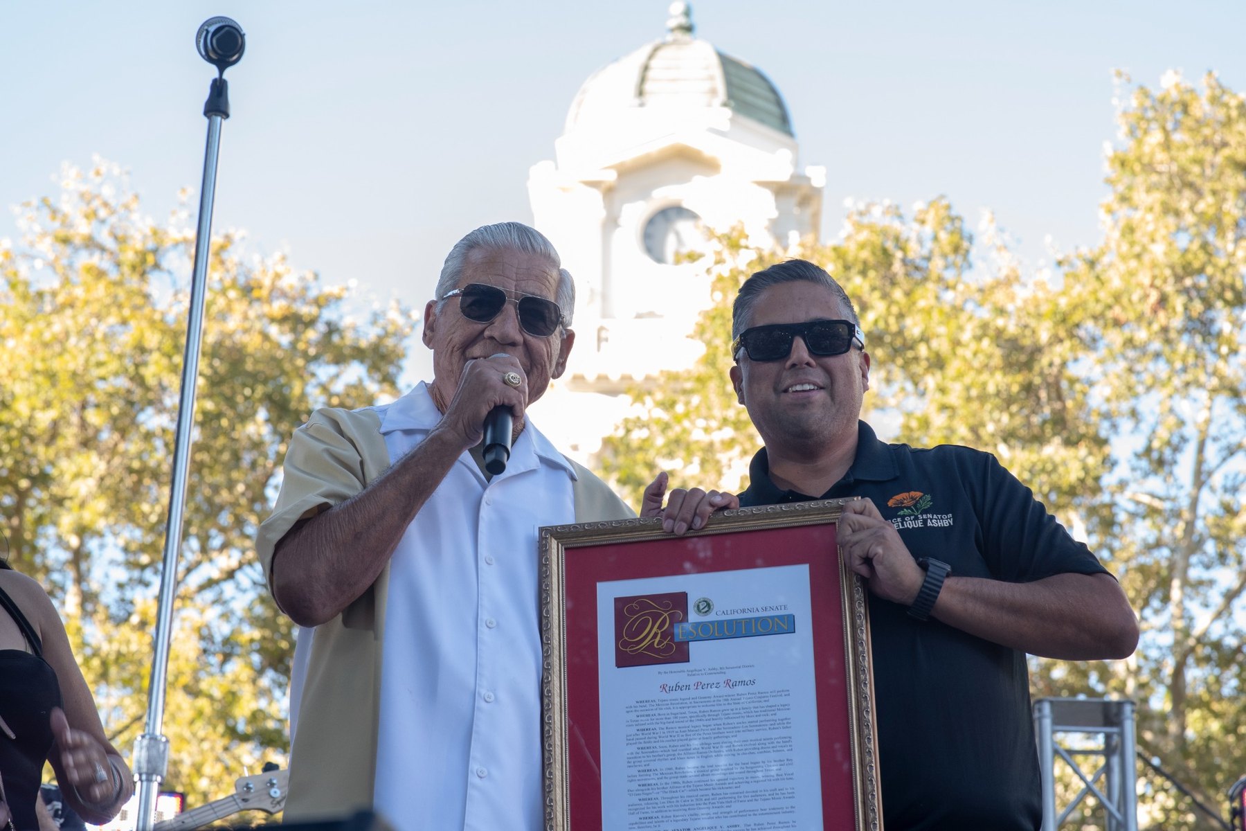 Ruben Ramos holding a framed California Senate Resolution onstage at the 2026 Tejano Conjunto Festival in Sacramento